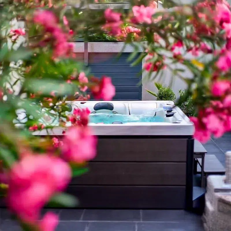 Spa Barthélemy vu à travers des fleurs roses, installé sur une terrasse en carrelage noir – Only Spa
