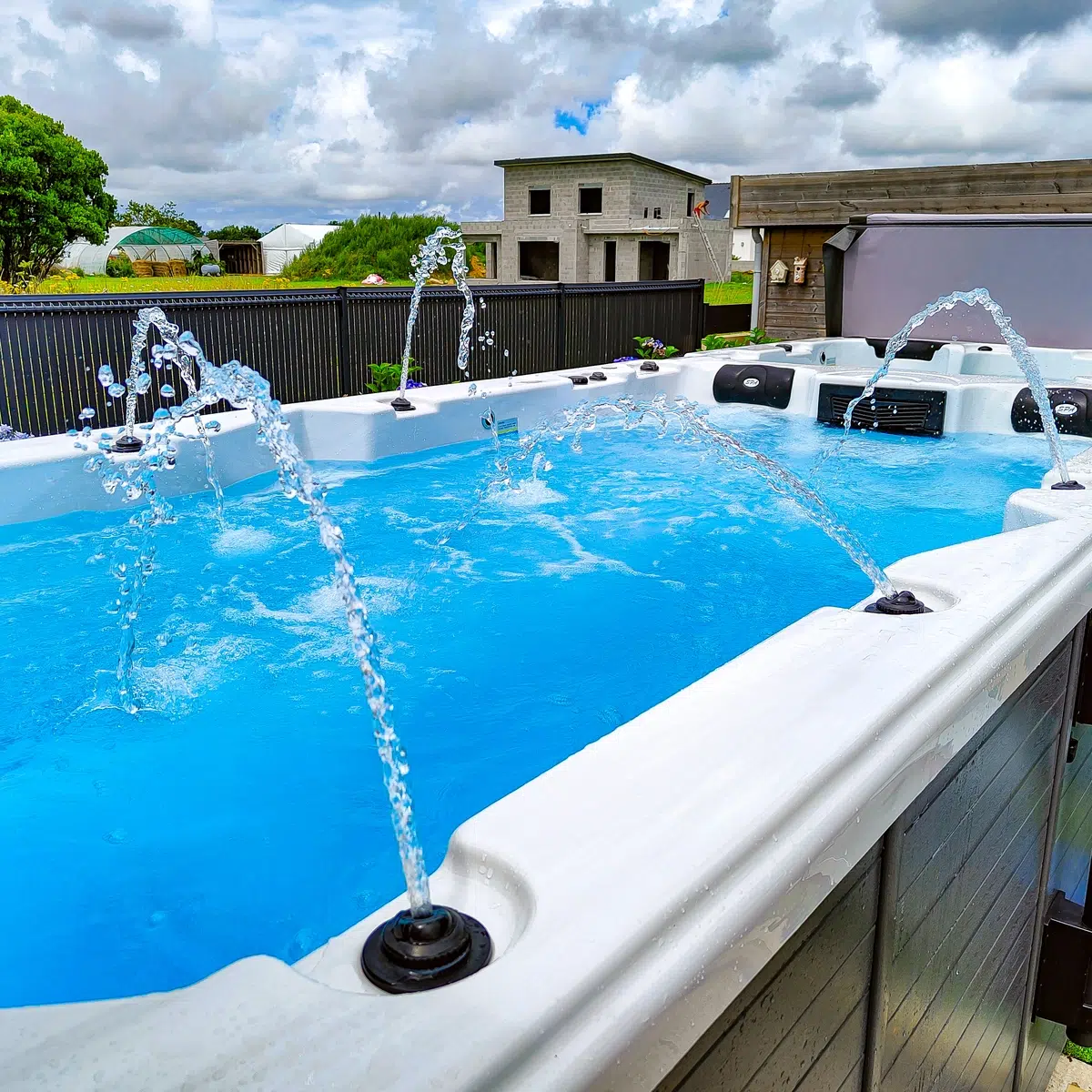 Spa de nage bi-zone Vendom Nisia installé en extérieur, avec jets d’eau activés et ciel nuageux en arrière-plan