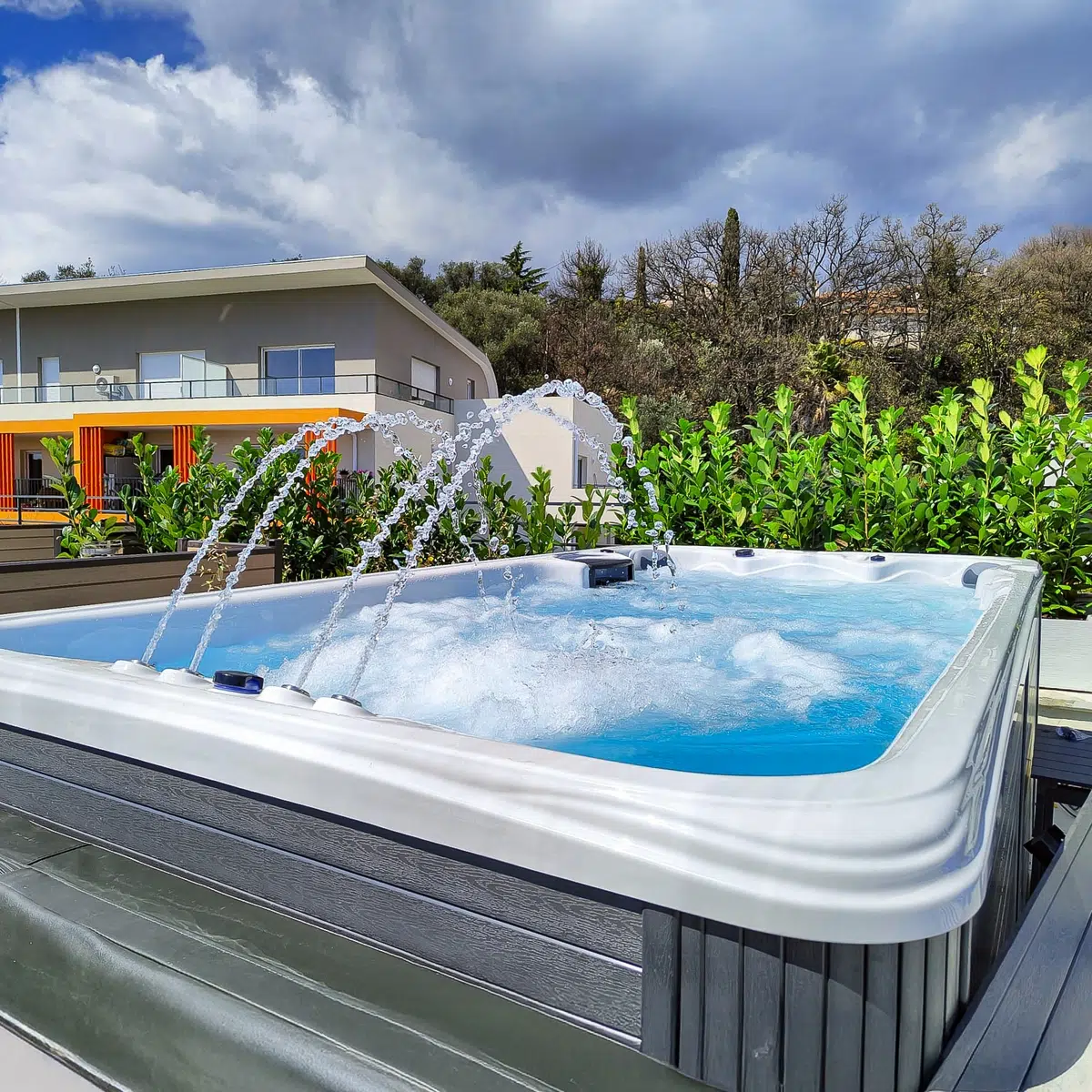 Le spa de nage Tilos de Vendom en pleine utilisation, avec jets massants activés et panorama côtier en arrière-plan