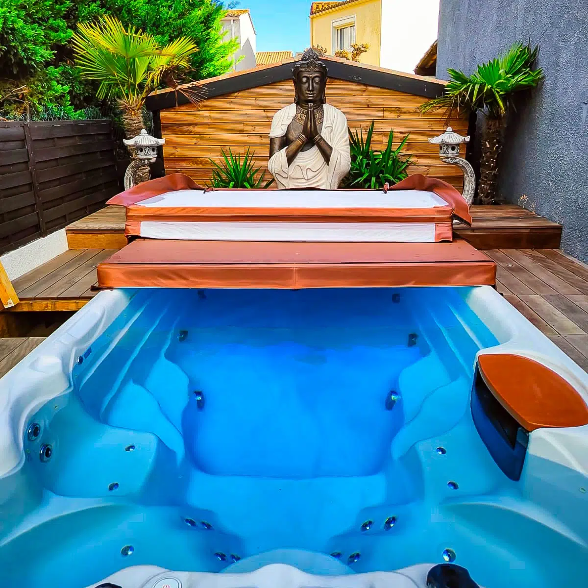 Spa de nage monobassin Tilos de Vendom dans un espace zen extérieur, encadré par une statue de Bouddha et des éléments asiatiques